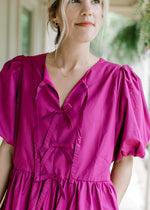 Close up of bow detail, pleated shoulders and short puff sleeves on a magenta dress. 