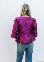 Back view of Model wearing a bubble 3/4 sleeve top with magenta flowers and peplum fit.