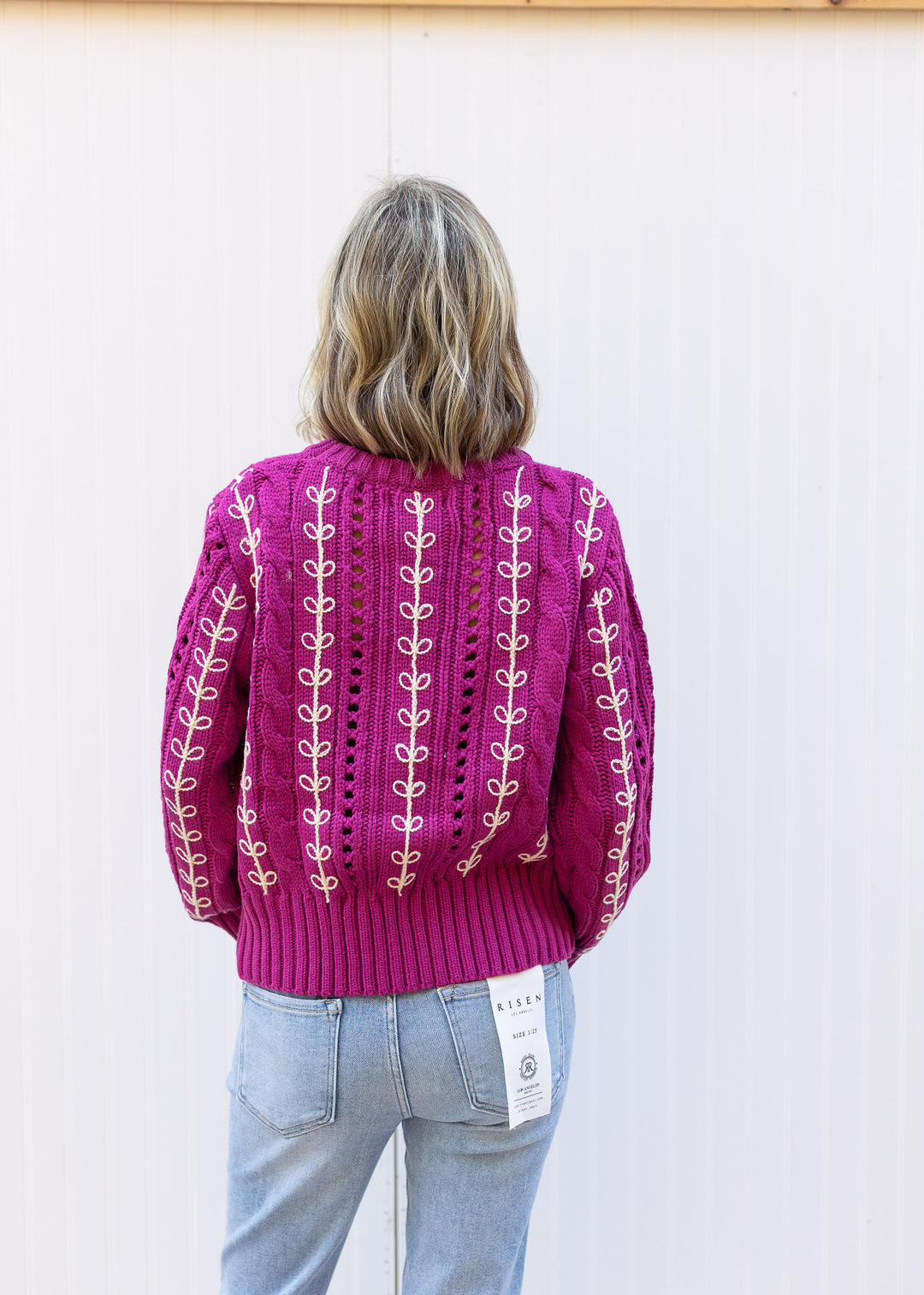Back view of Model wearing an openwork knit magenta sweater with cream embroidery.