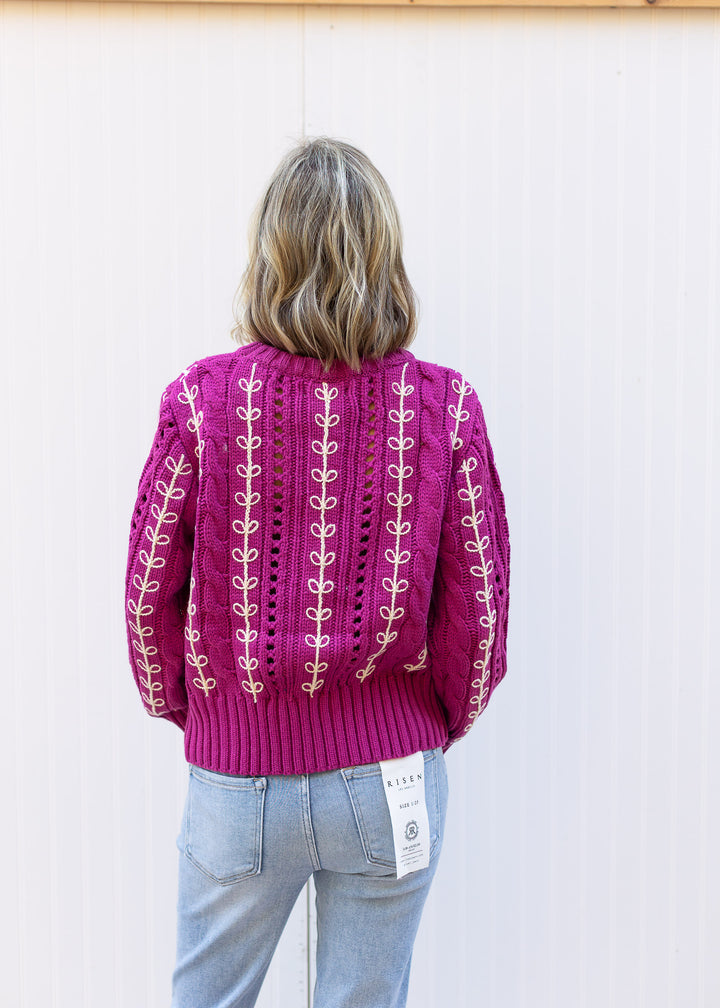 Back view of Model wearing an openwork knit magenta sweater with cream embroidery.