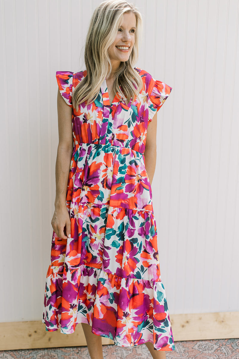 Model wearing a white dress with magenta flowers, ruffle cap sleeve, v-neck and elastic waist.