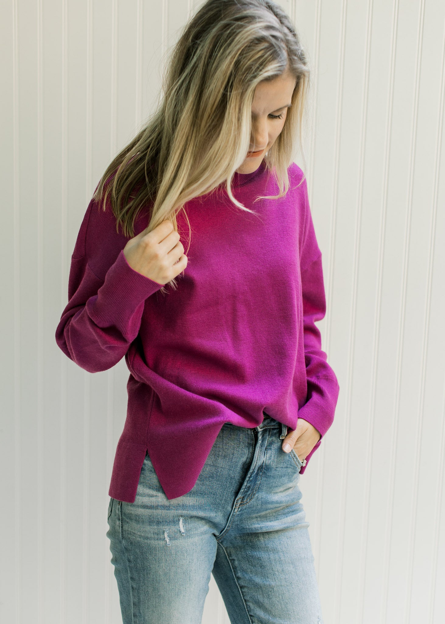 Model wearing a magenta long sleeve sweater with a mock neckline and split sides. 