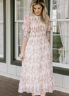 Model wearing a cream midi with a dusty mauve floral print, 3/4 poet sleeves and a smocked bodice.