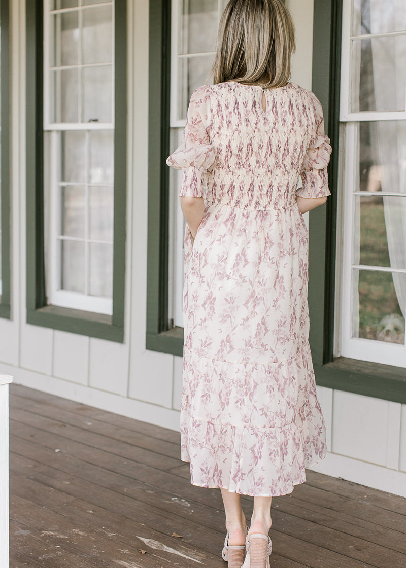 Back view of Model wearing a cream midi with mauve floral, 3/4 sleeves and a smocked bodice.