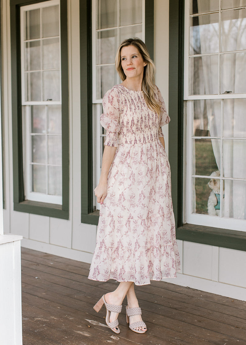 Model wearing heels and a cream midi with a mauve floral, 3/4 sleeves and a smocked bodice.