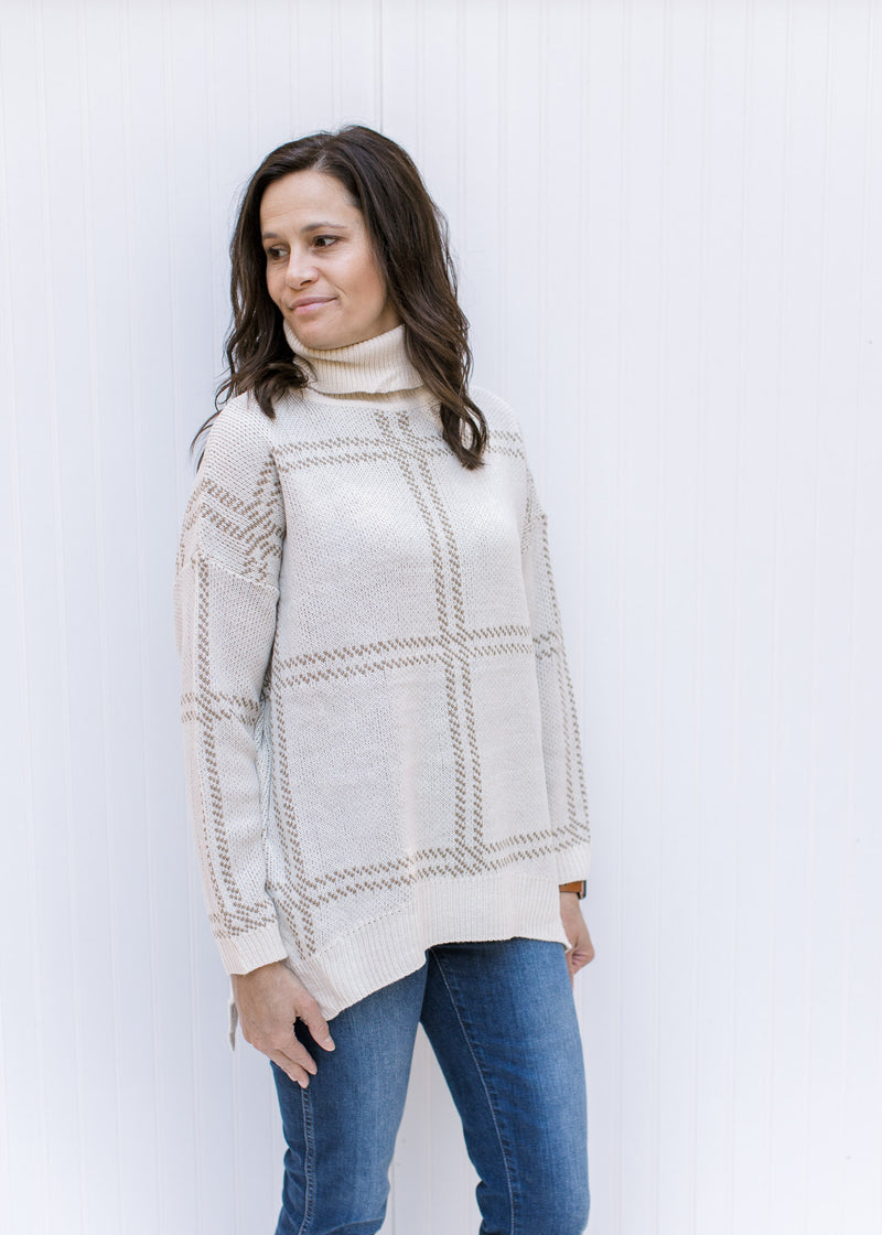 Model wearing a camel on cream plaid sweater with a turtleneck, split sides and long sleeves. 