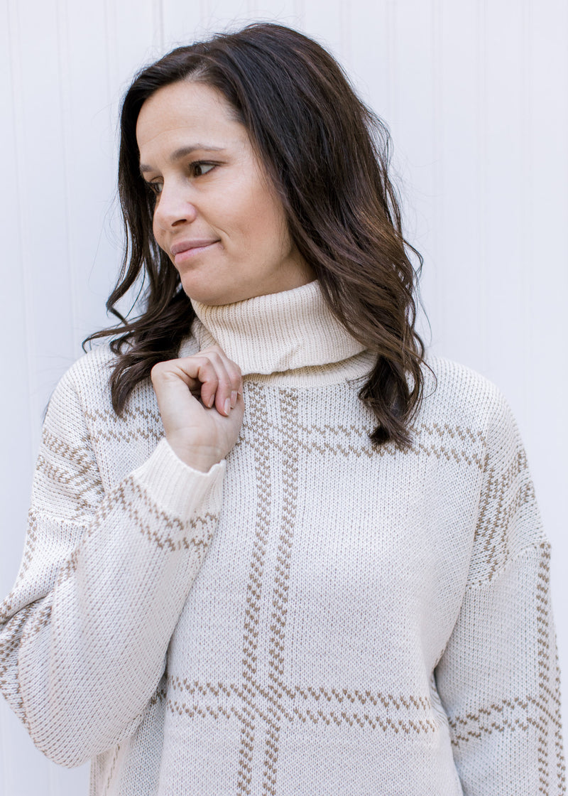 Close up of turtleneck on a cream and camel plaid sweater with split sides and long sleeves. 