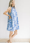 Model wearing a white sleeveless button up dress with a blue animal and tree print. 