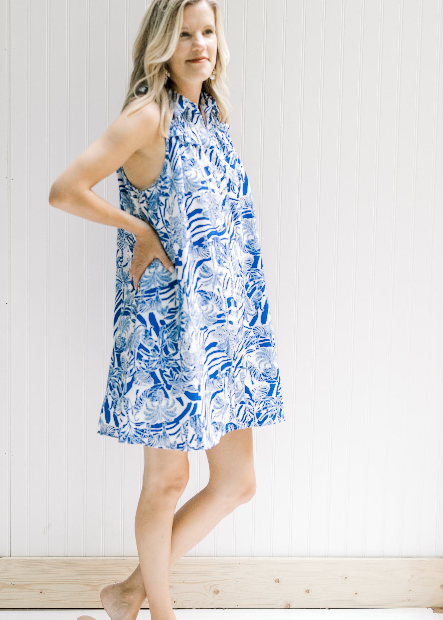 Model wearing a white sleeveless button up dress with a blue animal and tree print. 