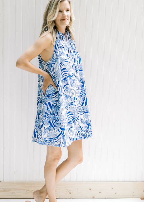 Model wearing a white sleeveless button up dress with a blue animal and tree print. 