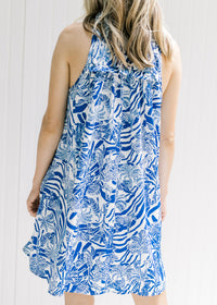 Back view of Model wearing a white sleeveless button up dress with a blue animal and tree print