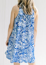 Back view of Model wearing a white sleeveless button up dress with a blue animal and tree print