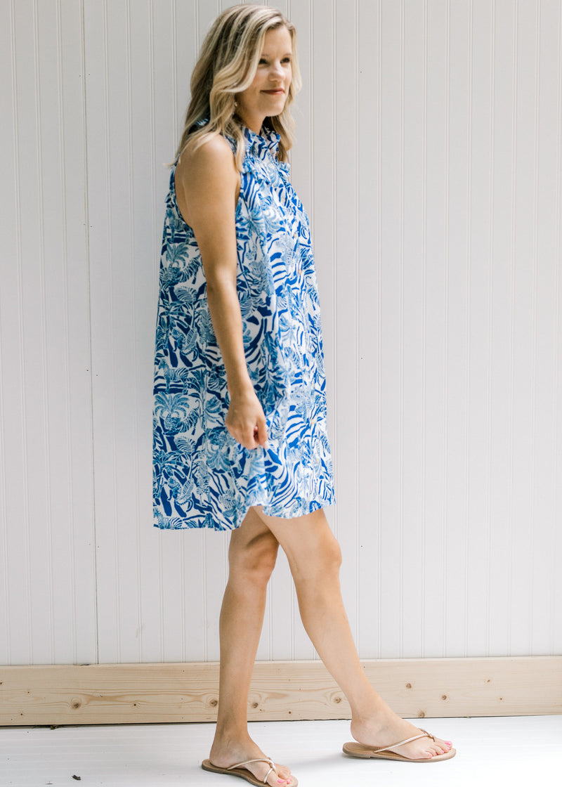 Model wearing sandals with a white sleeveless button up dress with a blue animal and tree print