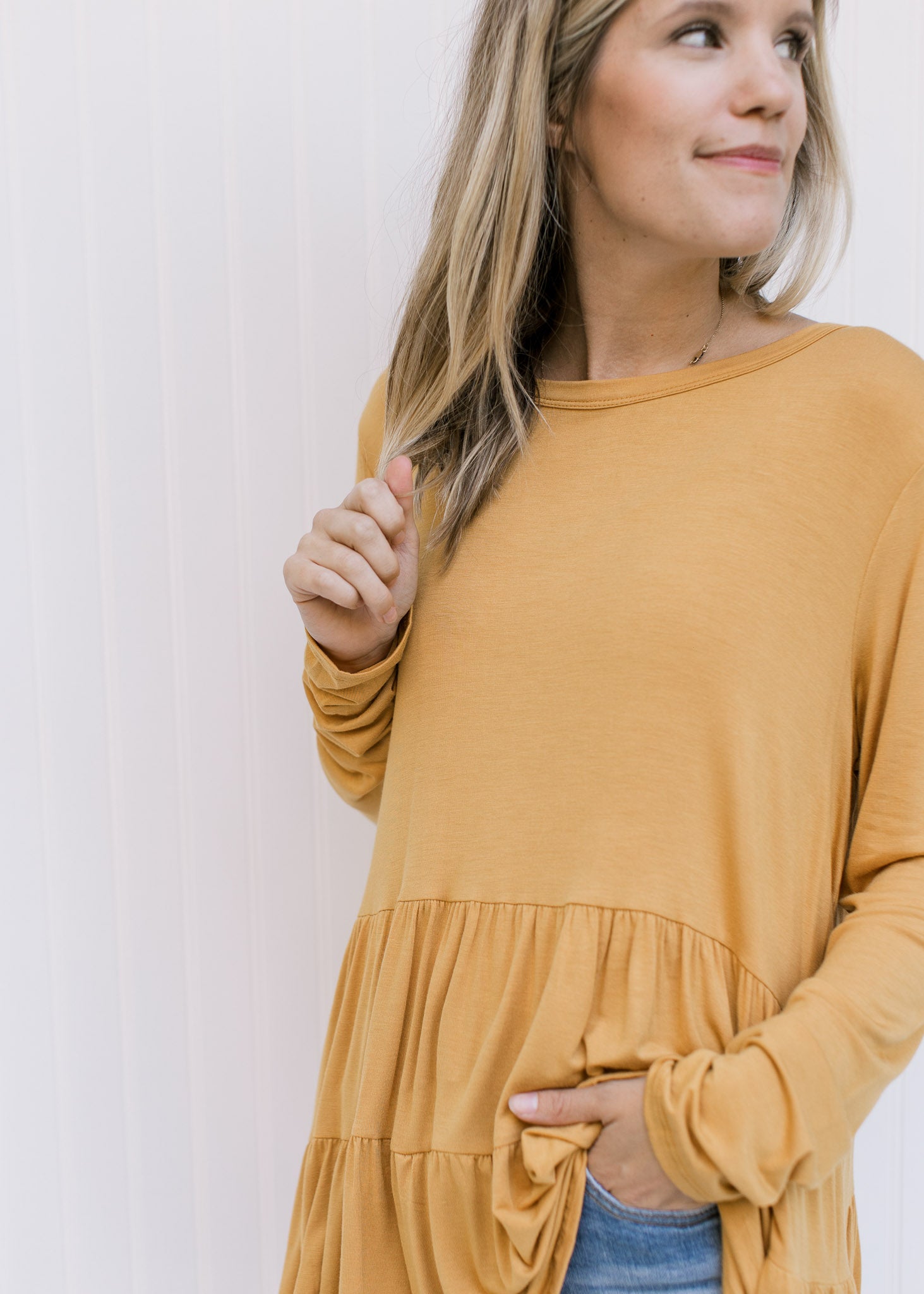 Close up of the tiers on a marigold colored top composed of a bamboo material with long sleeves. 