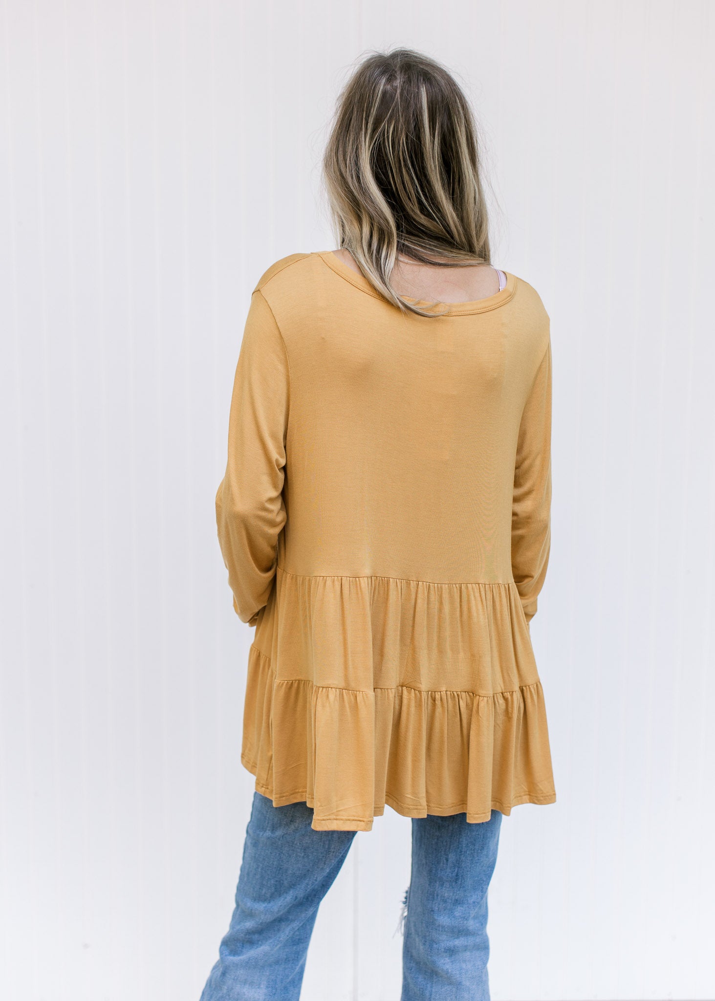 Back view of Model wearing a marigold, tiered top comprised of a bamboo material and long sleeves. 