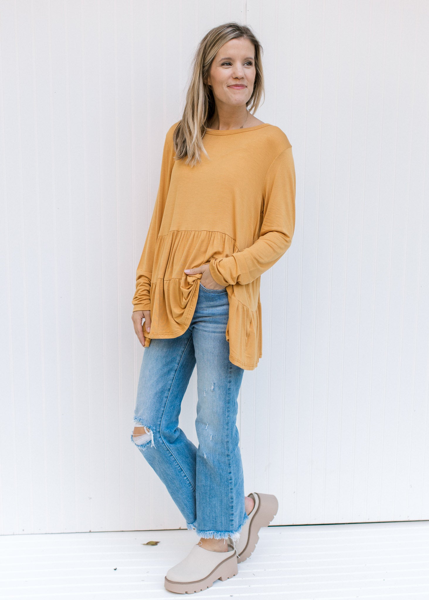 Model wearing jeans, mules and a marigold bamboo top with tiers and long sleeves. 