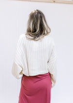 Back view of Model wearing a cream sweater over a soft maroon colored, short sleeve maxi dress. 