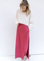 Model wearing a soft maroon colored maxi with split side hem a pull over cream sweater and booties. 