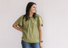 Model wearing jeans and an olive top with a braided neck detail and batwing short sleeves.