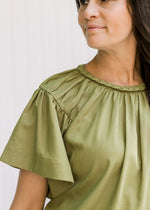 Close up view of braided detail on round neck of an olive top with batwing short sleeves.