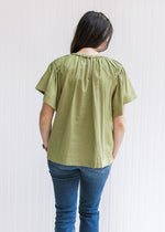 Back view of Model wearing an olive top with a keyhole closure, braided neck detail and short sleeve