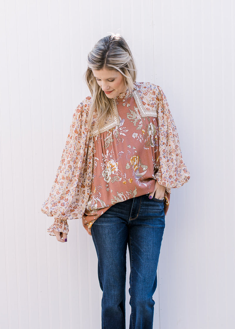 Model wearing jeans and a mauve mixed floral top with sheer long bubble sleeves with elastic cuff. 