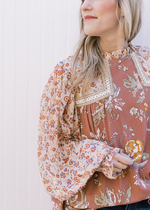 Model wearing a mauve mixed floral top with sheer long bubble sleeves with elastic cuff. 