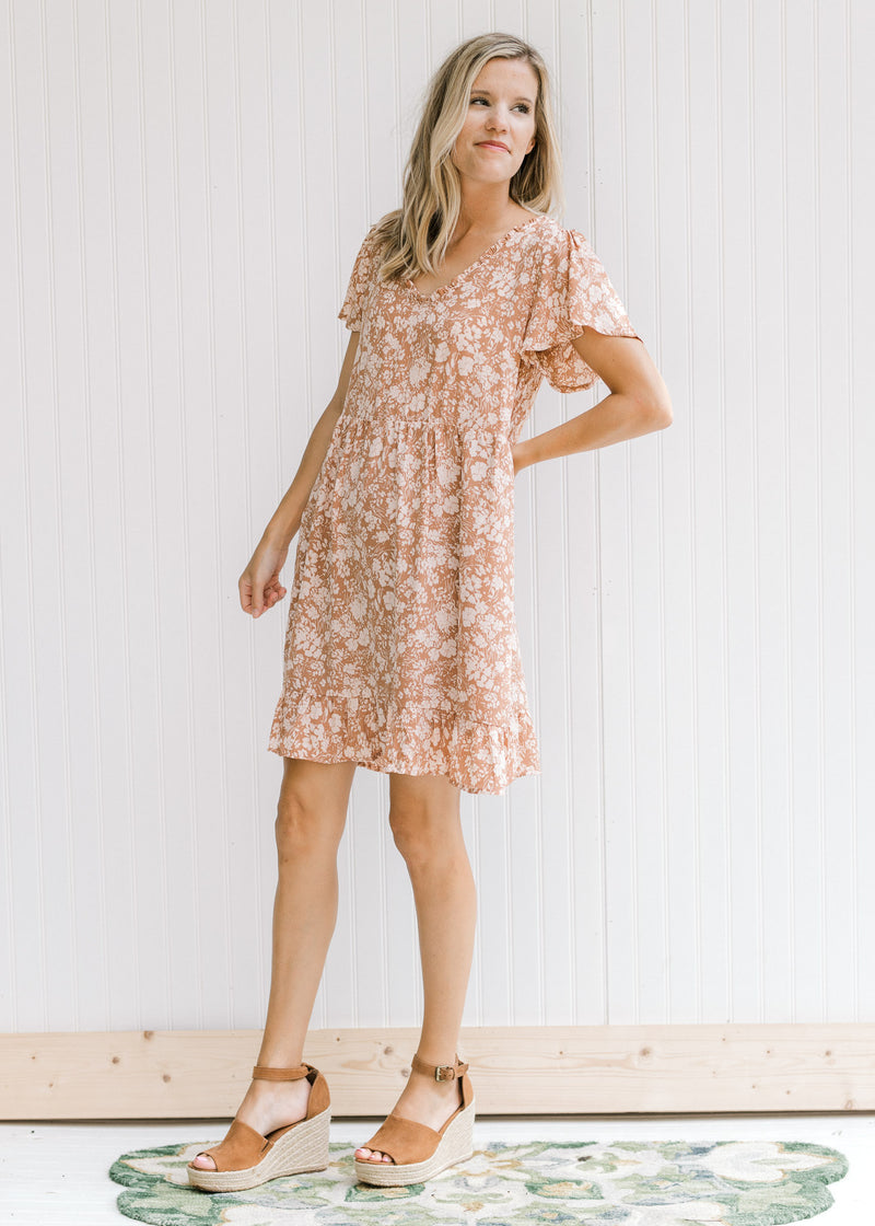 Model wearing wedges with a mauve dress with a cream floral, v-neck with ruffle and short sleeves.
