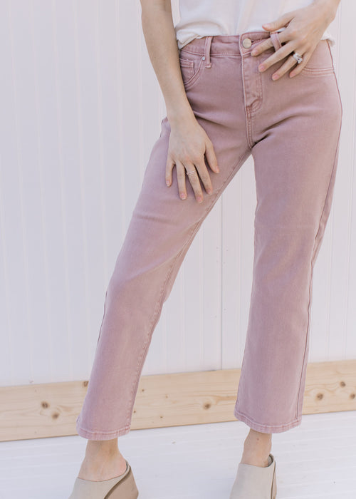 Model wearing mauve mid rise jeans with a cropped fit and button/zip closure.