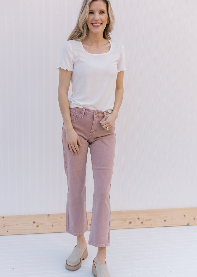 Model wearing a white ribbed top with mauve mid rise cropped jeans with a button/zip closure.