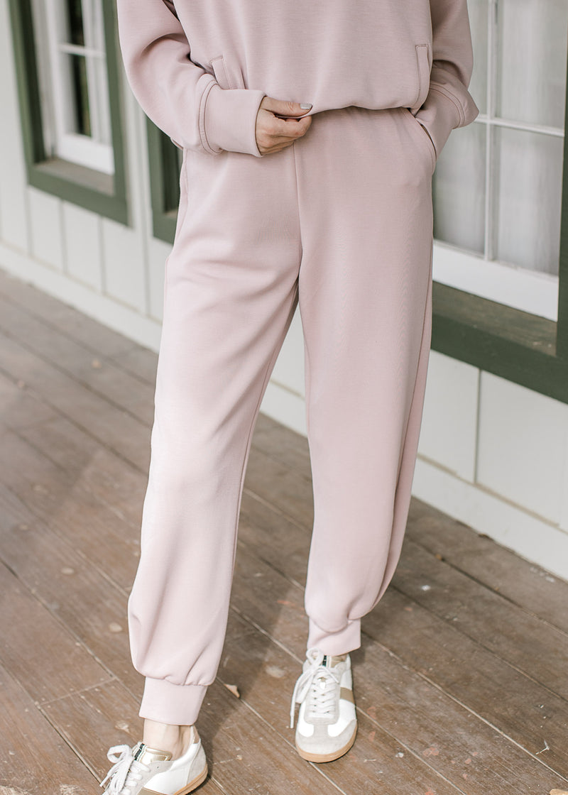 Close up of mauve joggers with pockets, elastic waist and a matching quarter zip top. 