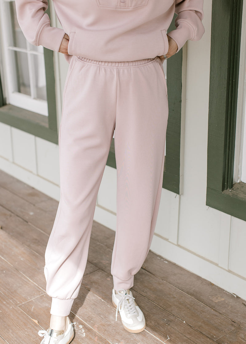 Model wearing sneakers and mauve joggers with pockets, elastic waist and a matching top. 