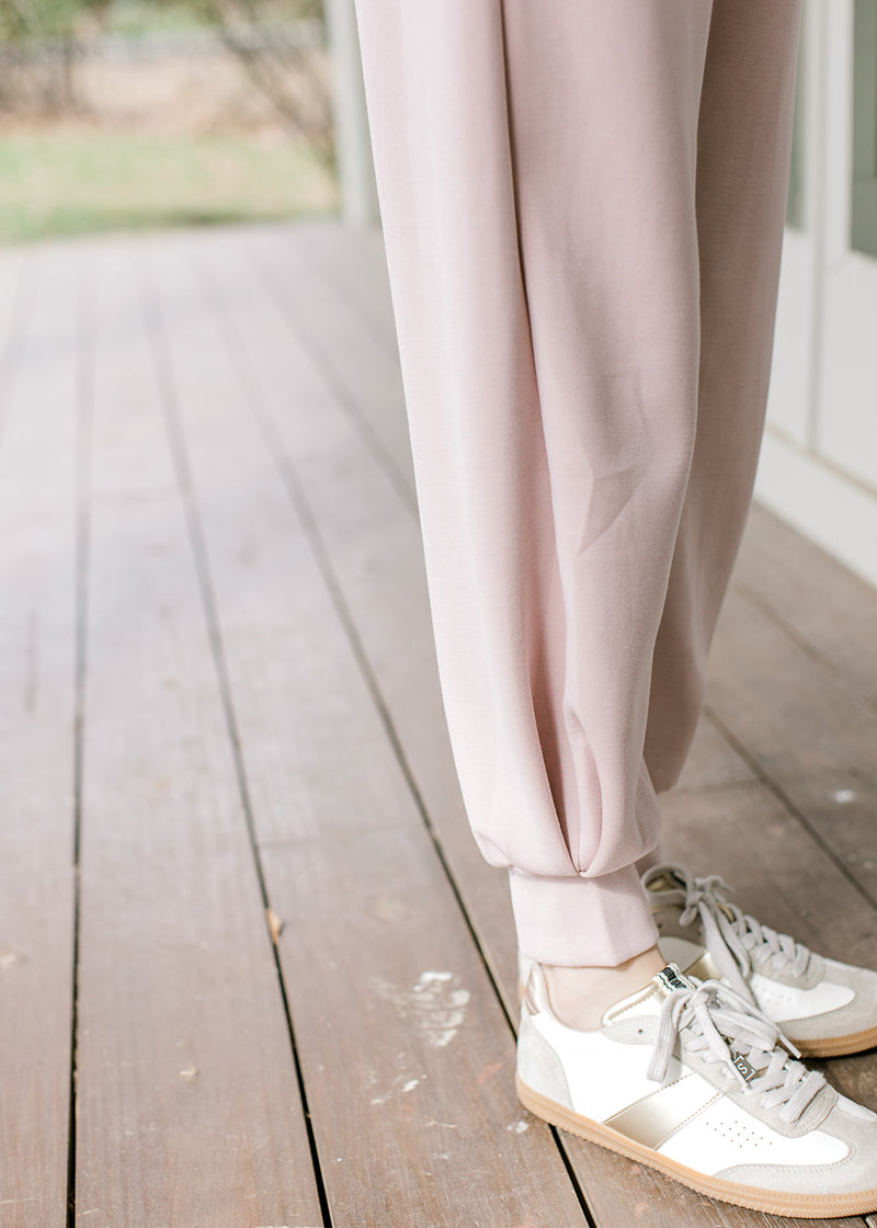 Close up of jogger fit on mauve pants with pockets, elastic waist and a matching quarter zip top. 