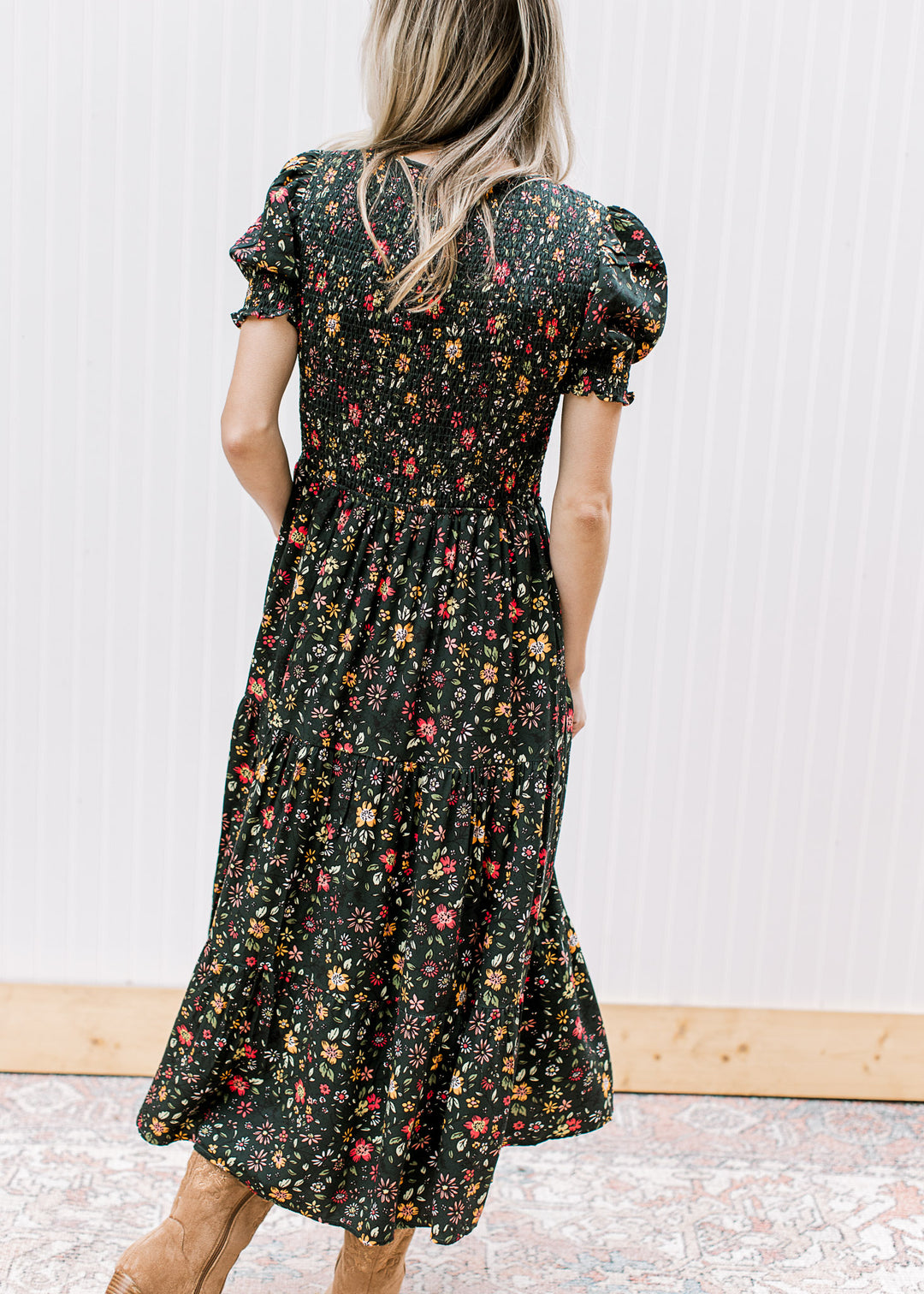 Back view of Model wearing a hunter green midi with warm floral, smocked bodice, and short sleeves.