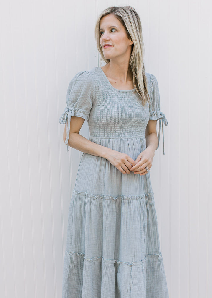 Model wearing a pale blue midi with gauze fabric, smocked bodice and short sleeves with tie detail. 