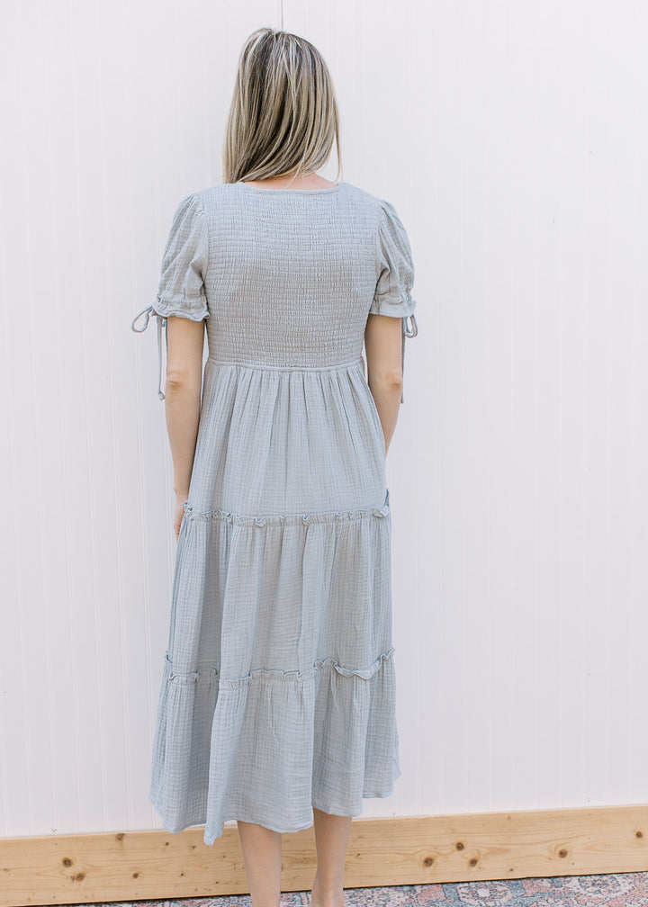 Back view of Model wearing a pale blue midi with smocked bodice and short sleeves with tie detail. 
