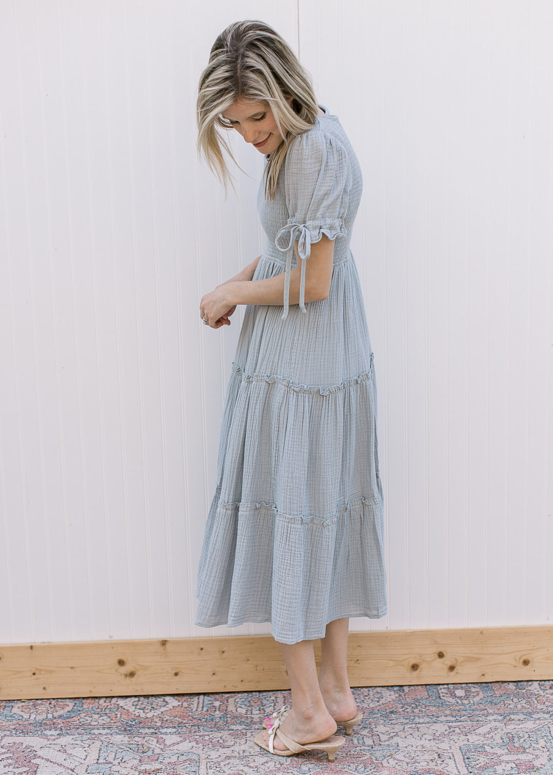 Model wearing sandals and a pale blue midi with smocked bodice and short sleeves with tie detail.