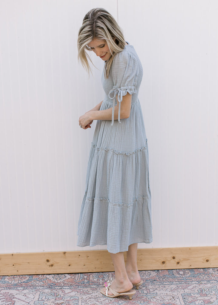Model wearing sandals and a pale blue midi with smocked bodice and short sleeves with tie detail.