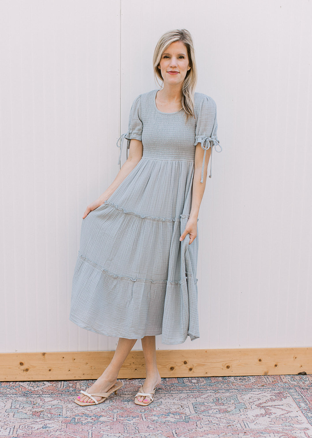 Model wearing a pale blue midi with tiered skirt, smocked bodice and short sleeves with tie detail. 