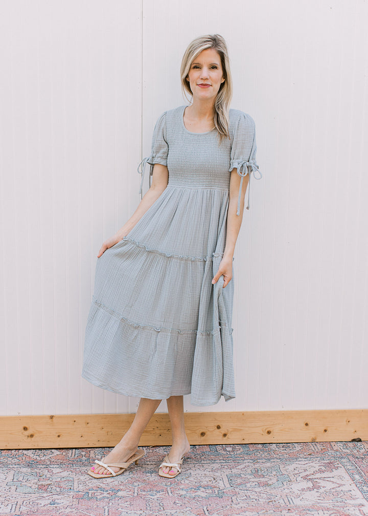Model wearing a pale blue midi with tiered skirt, smocked bodice and short sleeves with tie detail. 