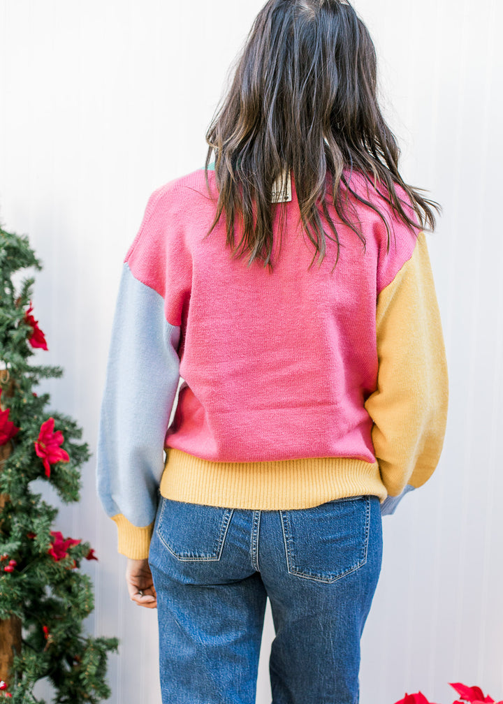 Back view of Model wearing a bright  “MERRY” sweater with a round neckline and long sleeves. 
