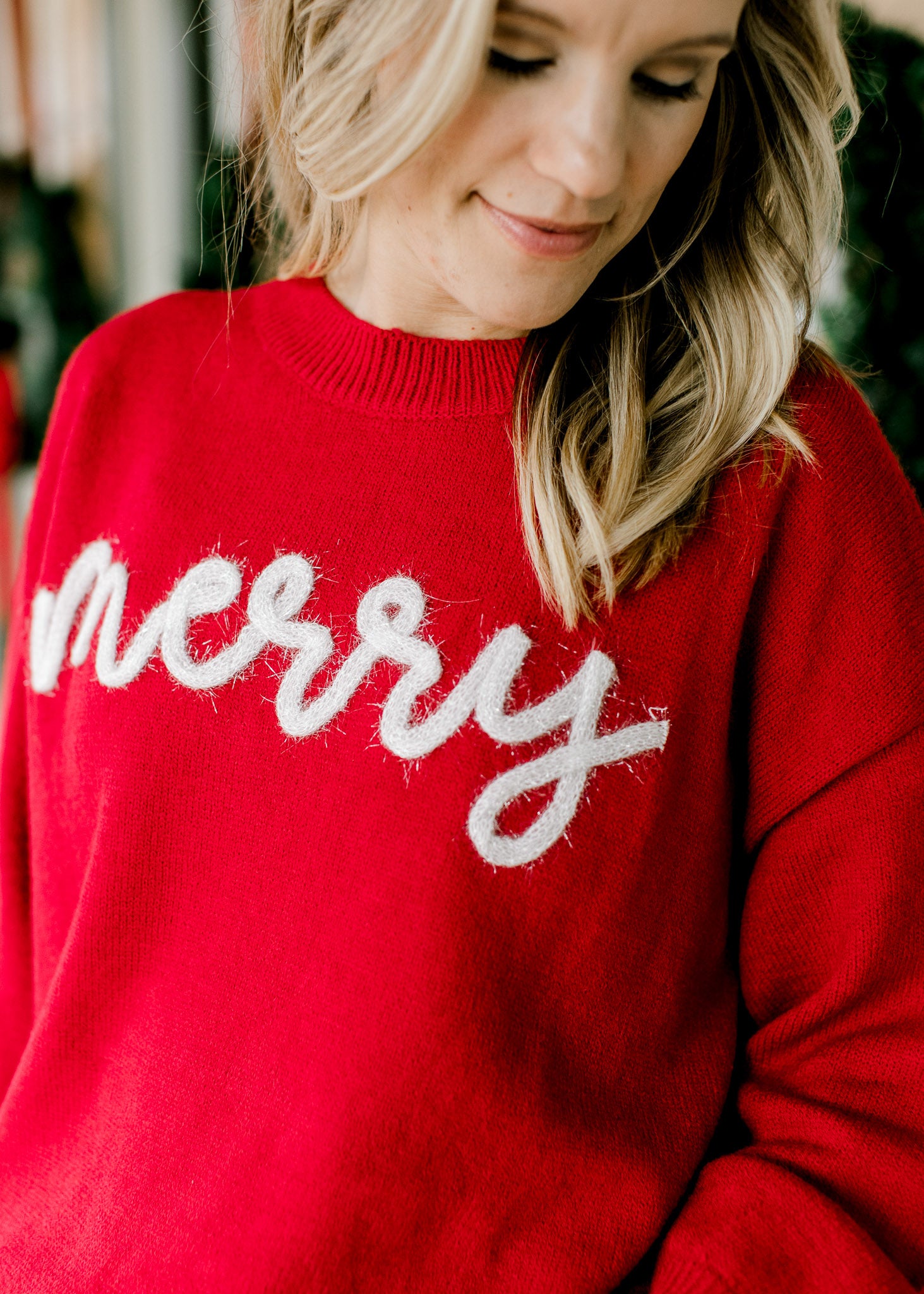 Close up of white merry in scripted letters across a long sleeve, round neck red sweater. 