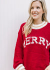 Model wearing a red long sleeve sweater with “MERRY” across the front in cream font. 