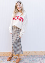 Model wearing a plaid skirt and cream sweater with MERRY in red yarn and long sleeves.