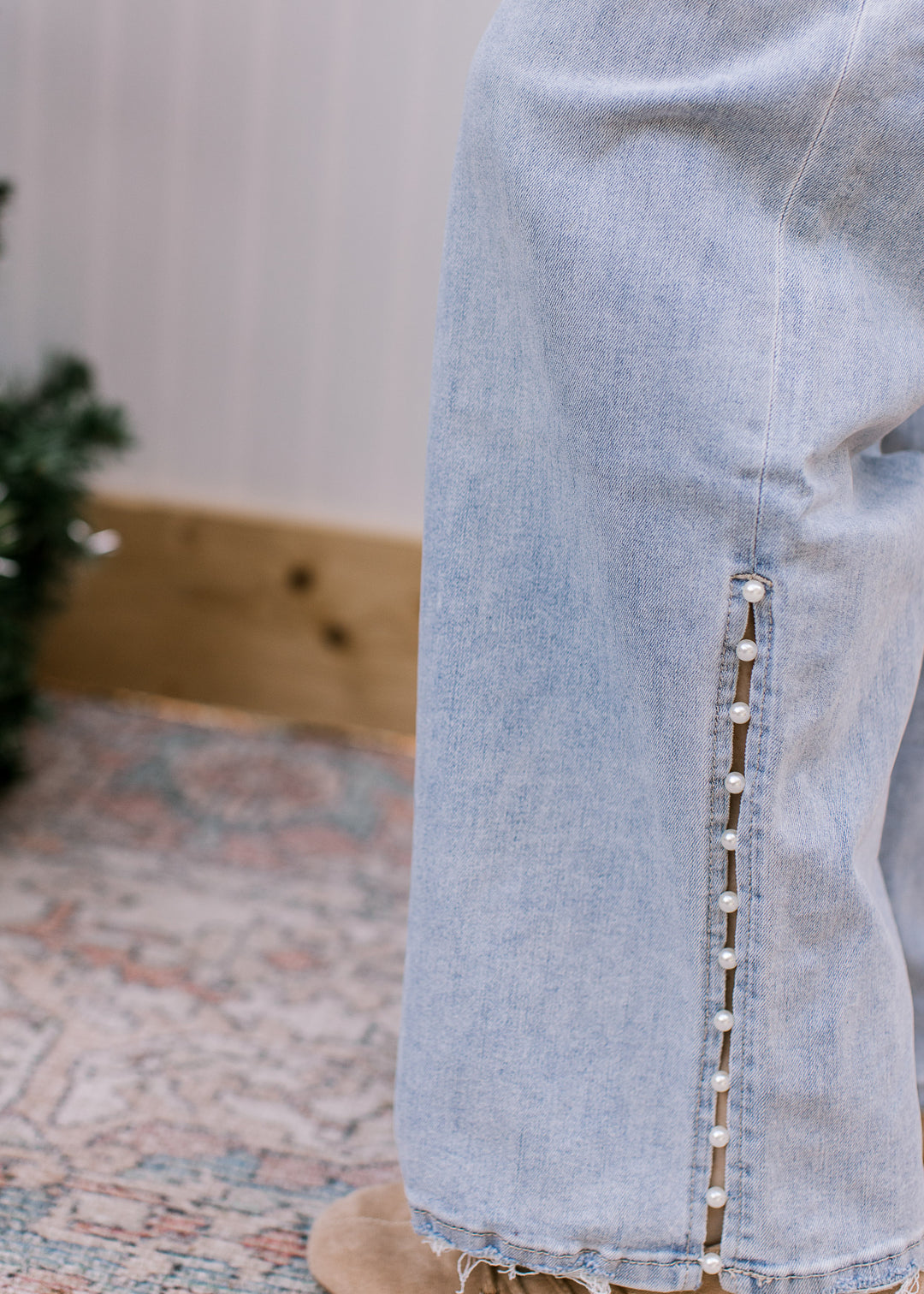 Close-up of Mica Denim light-wash jeans showing pearl embellishments along the lower side slit and frayed hem.