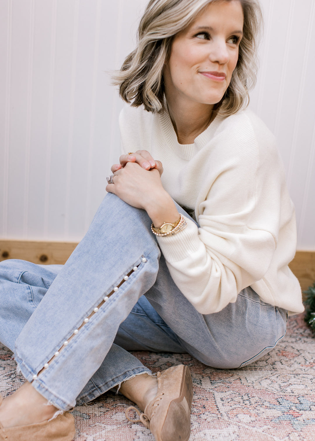 Seated model wearing Mica Denim light-wash wide leg jeans, showing pearl-trimmed side slits and frayed hems.