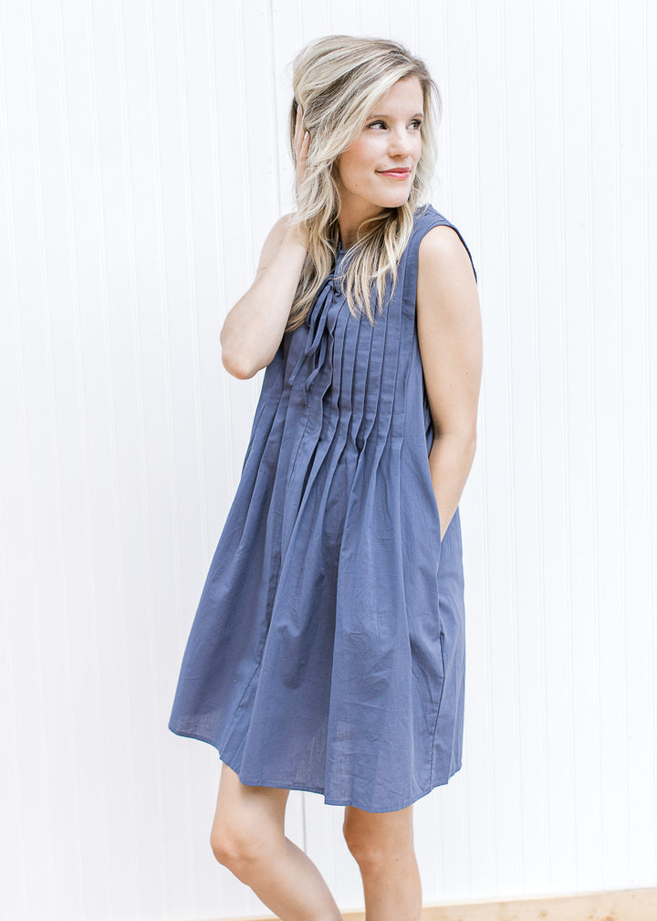 Model wearing a sleeveless navy above the knee dress with a pleated bodice and double tie v-neck.
