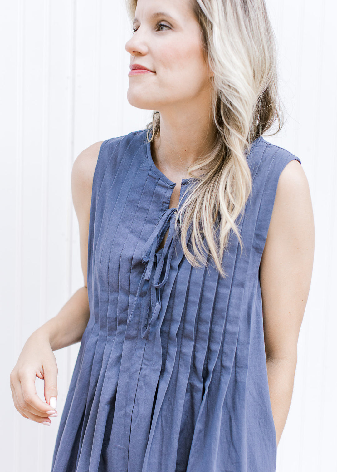 Close up of pleating and double tie v-neck on a sleeveless navy, above the knee dress. 