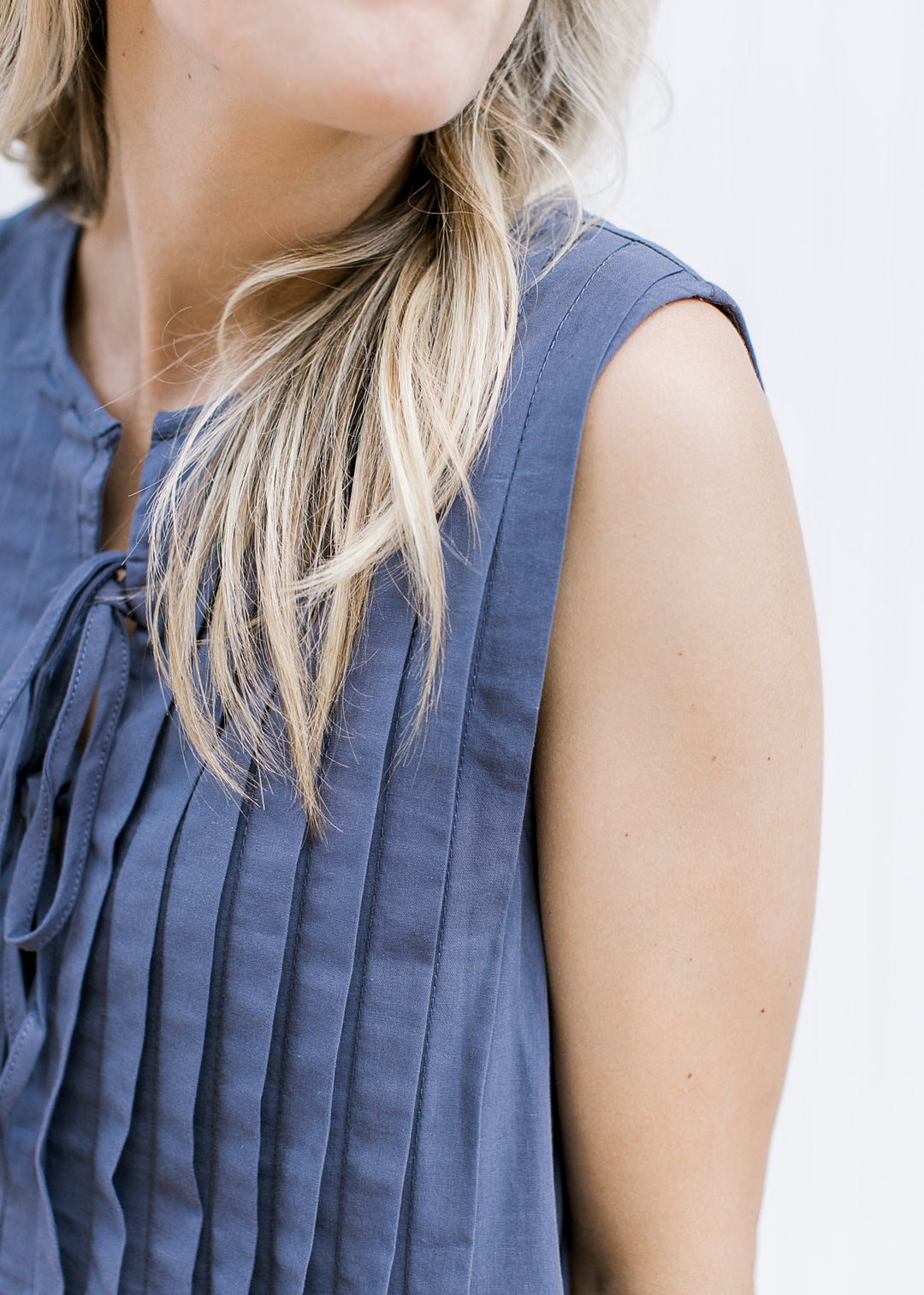 Close up of pleating on a navy sleeveless dress with a double tie v-neck and above the knee fit. 