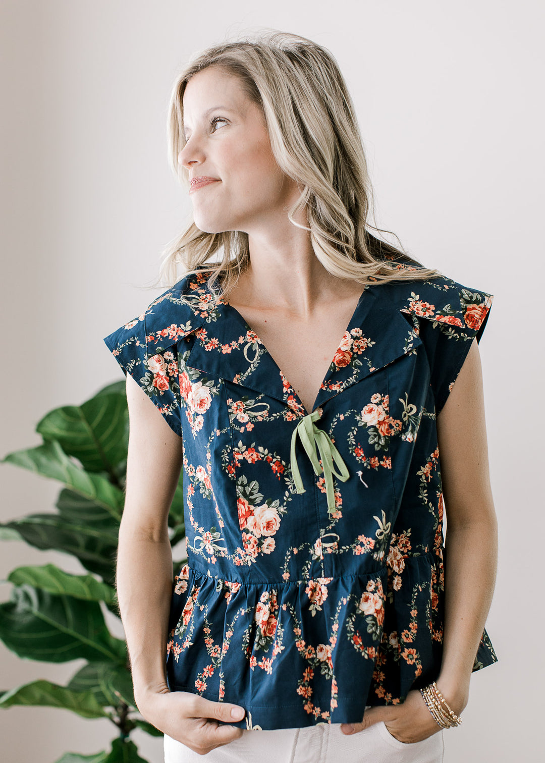 Model wearing a navy top with pink floral, v-neck with green bow, exaggerated collar and cap sleeve.